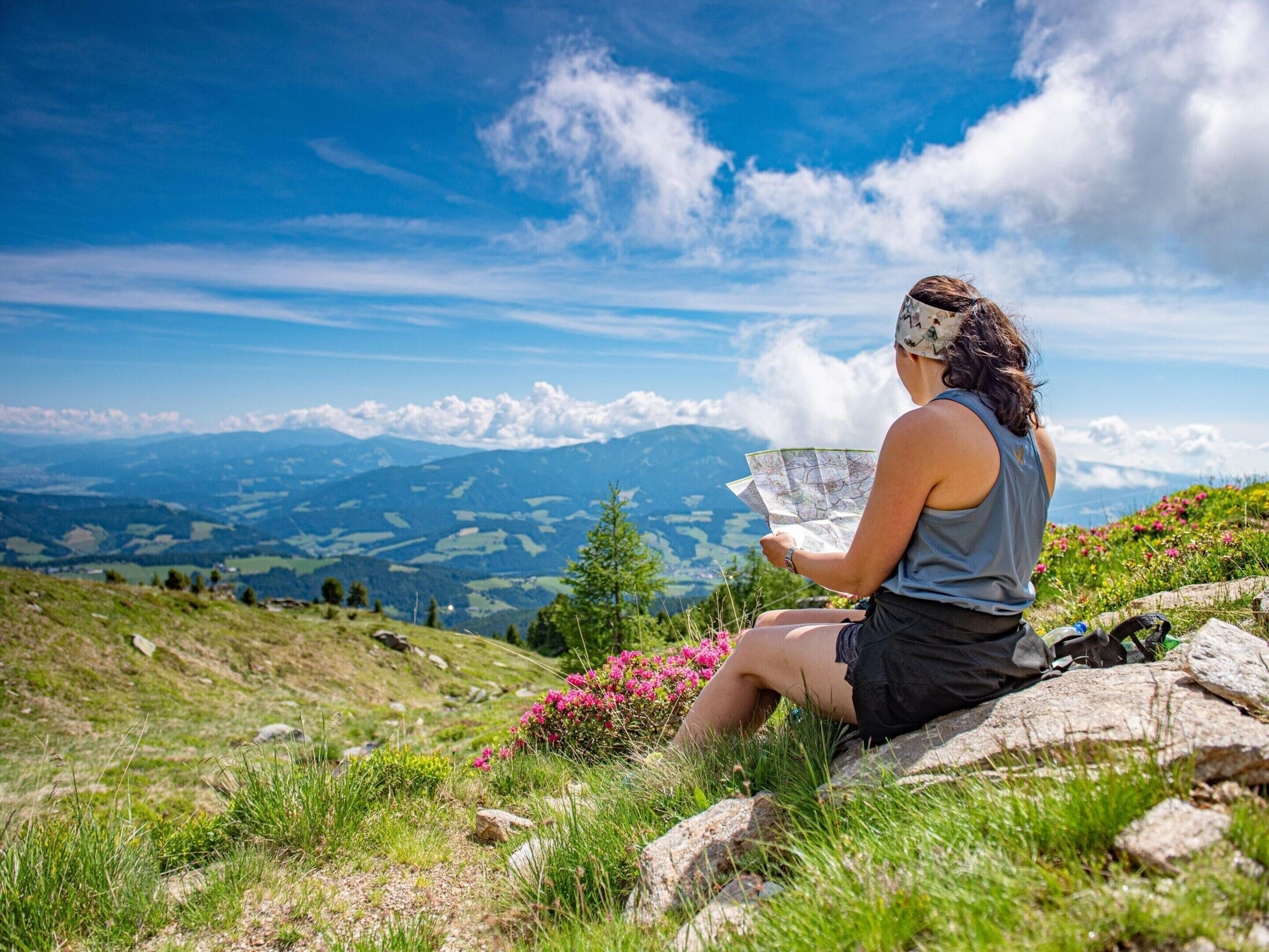 Una persona sentada sobre una roca con un mapa, contemplando un paisaje montañoso.