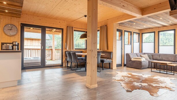 A spacious cabin interior with a dining area, seating, and a large window overlooking a deck. - Premium Chalet With Terrace (Hohentauern)