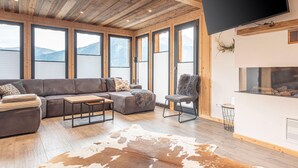 A modern living room with a wooden ceiling, large windows, a sectional sofa, a coffee table, a fireplace, and a mounted TV. - Premium Chalet With Terrace (Hohentauern)