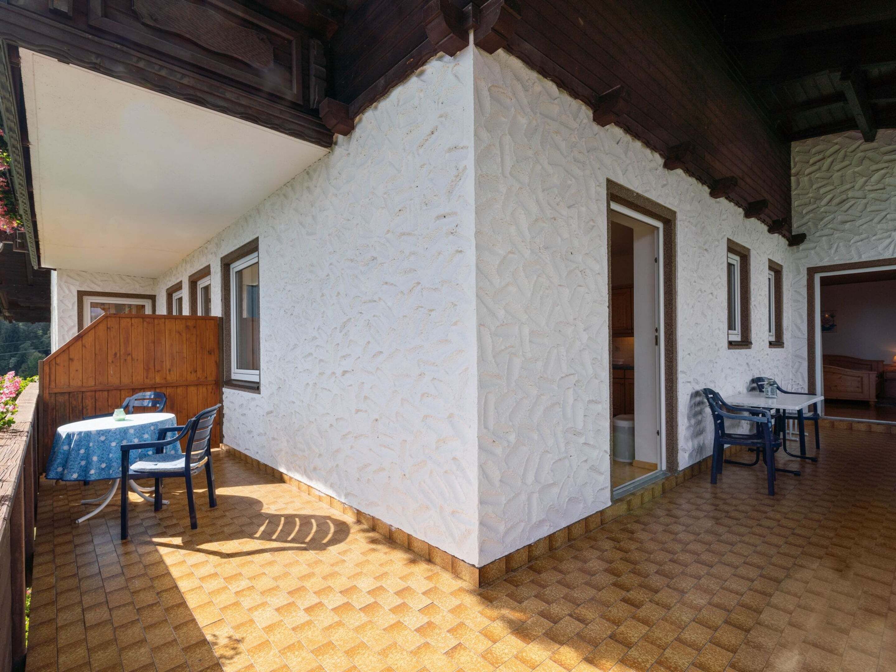 A covered patio area with a white textured wall, wooden ceiling beams, and a tiled floor.