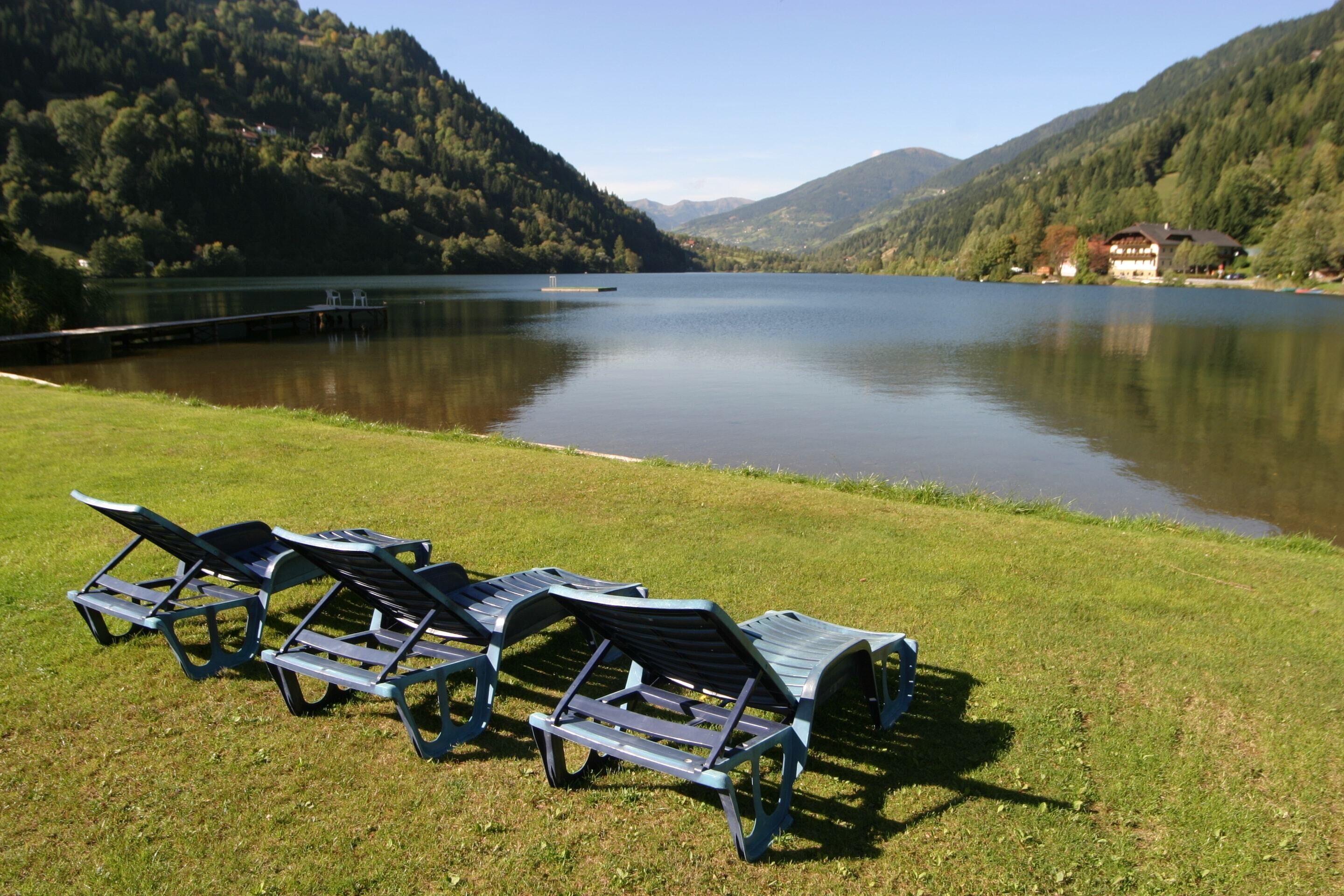 A lakeside view with lounge chairs and a building in the background. - Spacious Apartment in Afritz am See near Ski Area (Treffen)