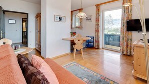 A cozy living room with a sofa, a dining table, and a TV. There's a wooden cabinet and a window with curtains. - Spacious Apartment in Afritz am See near Ski Area (Treffen)