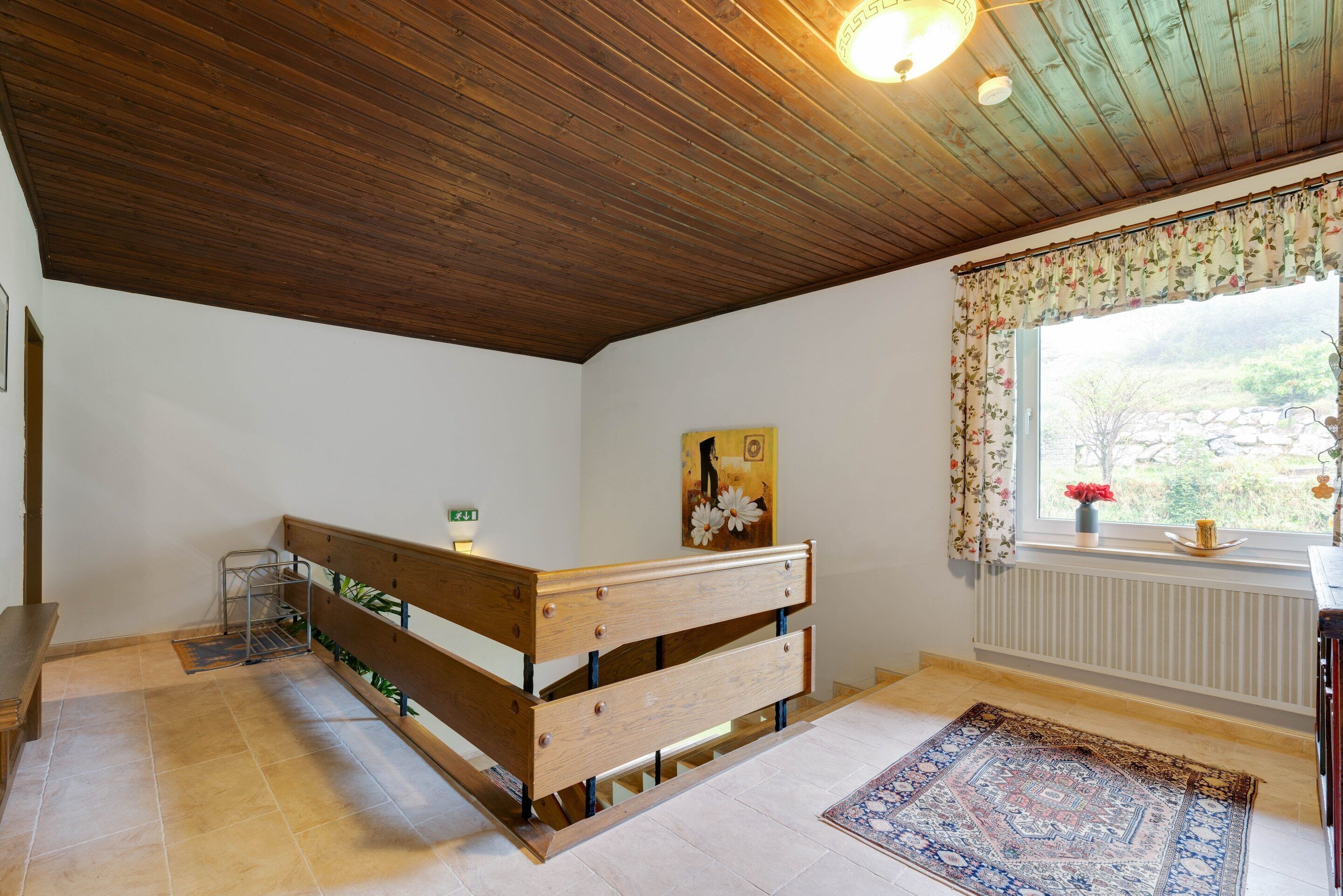 A room with a wooden bench, a radiator, a window with floral curtains, and a patterned rug.