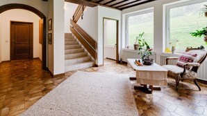 A spacious room with a wooden staircase, a large window with a view, and a cozy seating area with a chair and table. - Spacious Apartment in Afritz am See near Ski Area (Treffen)