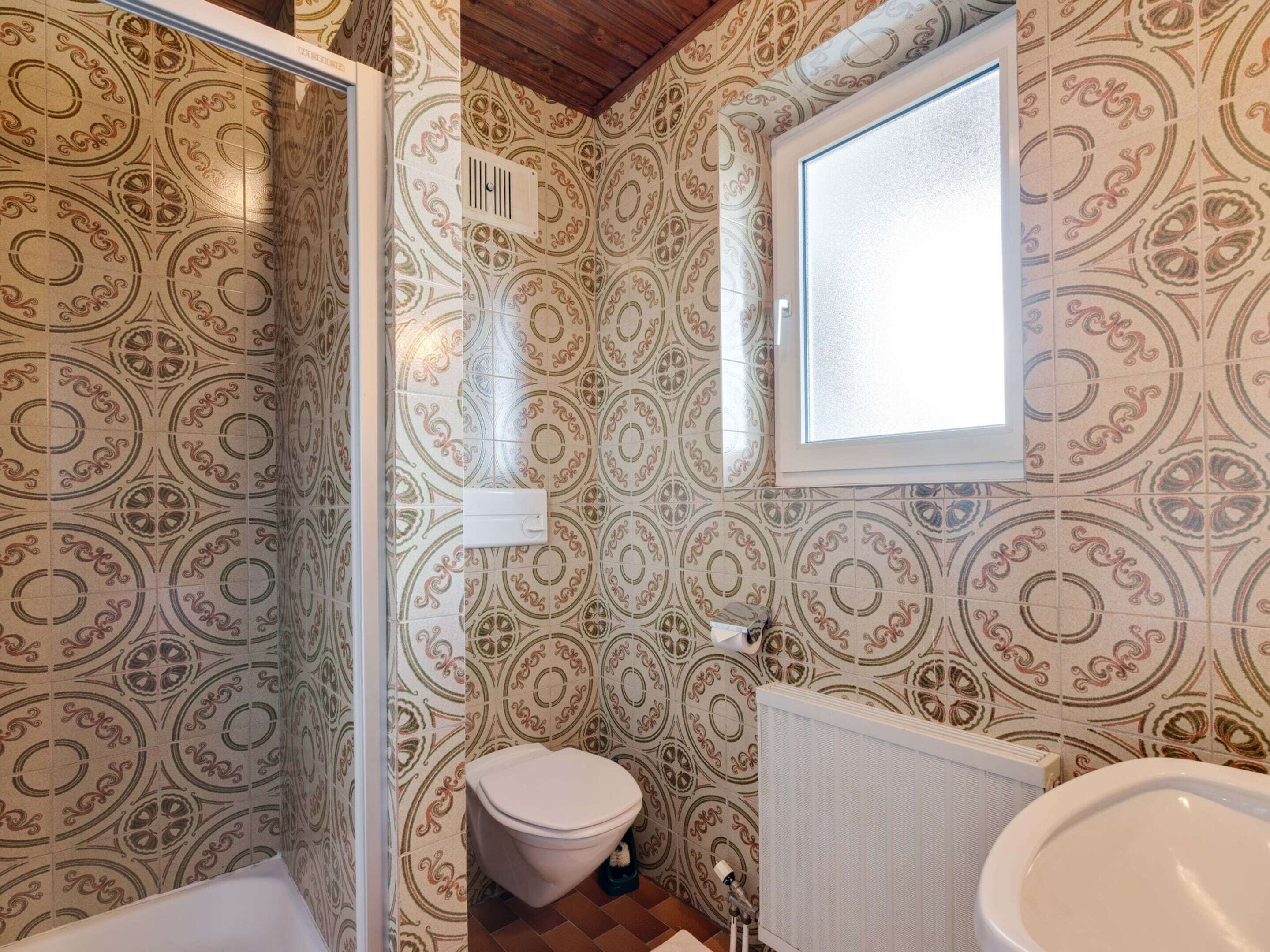 A bathroom with patterned tiles, a toilet, a sink, and a window.