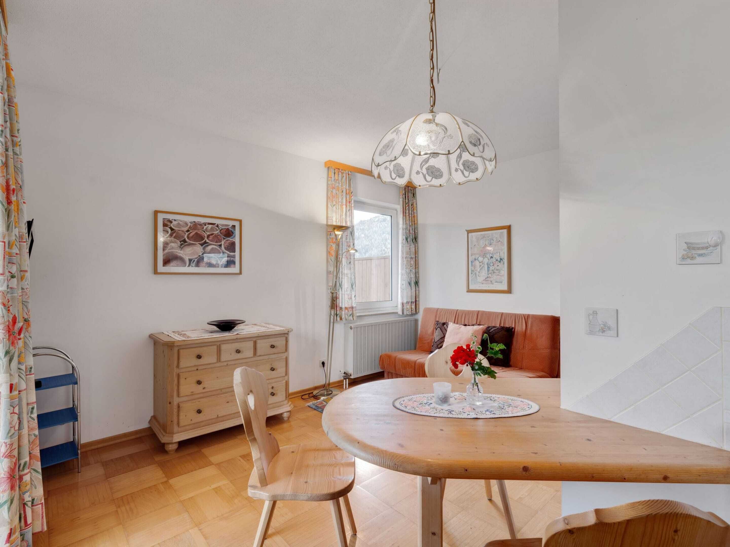 A dining area with a wooden table, chairs, a hanging light fixture, and a sofa.