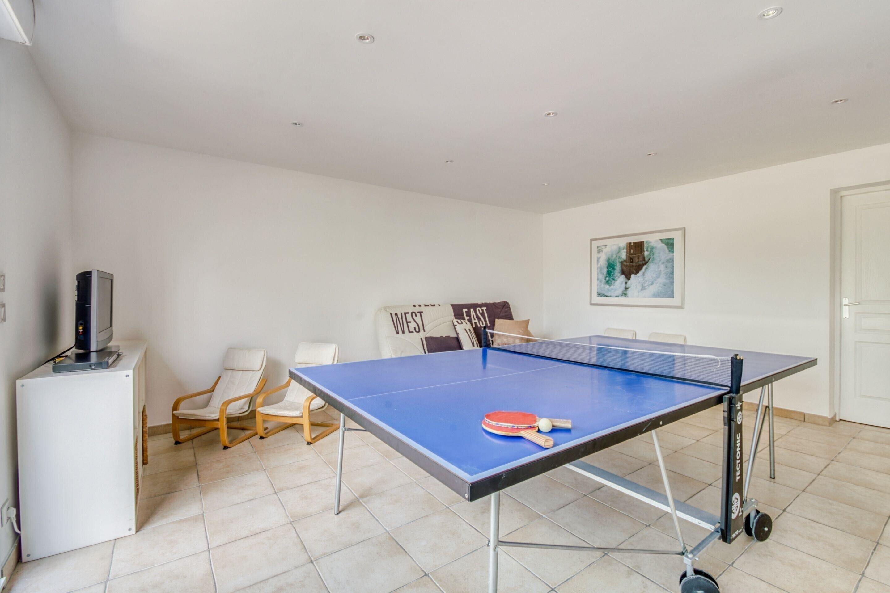A ping pong table with a table tennis paddle and ball, a white air conditioner, a wooden chair, and a white door.