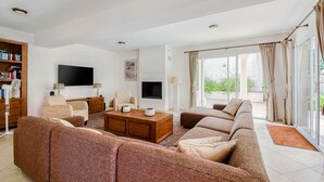 A spacious living room with a sofa set, a coffee table, a flat-screen TV, a bookshelf, and a large window with curtains. - Villa in Le Muy With Private Pool & Forest (Le Muy)