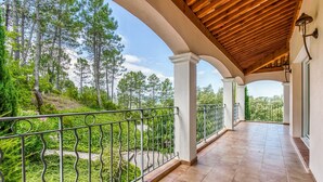 A covered balcony with a tiled floor, white pillars, and a metal railing overlooking a garden with trees and shrubs. - Villa in Le Muy With Private Pool & Forest (Le Muy)