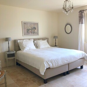 A bedroom with a bed, two bedside tables, a chandelier, a painting, a mirror, and a window with curtains. - Mas in Eygalieres With Heated Pool (Eygalieres)