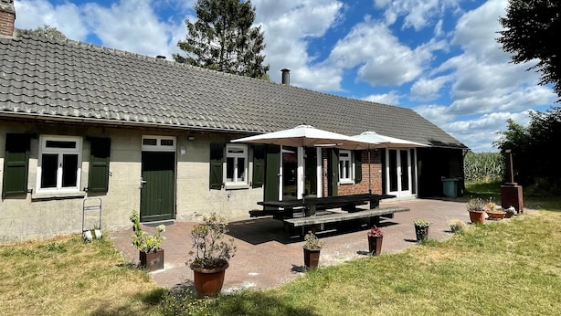 A building with a tiled roof, green shutters, and a covered patio area with benches. - Spacious Farmhouse near Forest in Stramproy (Stramproy)