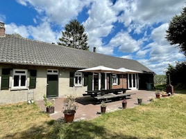 A building with a tiled roof, green shutters, and a covered patio area with benches.