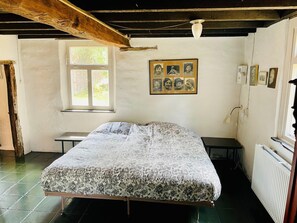 A bedroom with a bed, a window, a radiator, and a wall with framed photos.