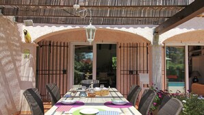 An outdoor patio with a table set for dining, surrounded by wicker chairs, and a pergola overhead. - Villa in Bagnols Near Sea With Pool (Bagnols-en-Foret)