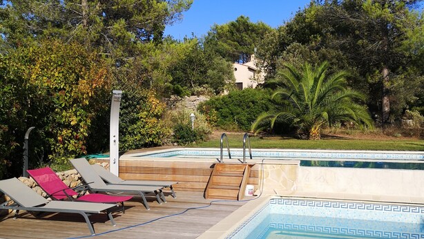A swimming pool with lounge chairs and a wooden deck, surrounded by trees and a building in the background. - Villa in Bagnols Near Sea With Pool (Bagnols-en-Foret)