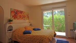 A bedroom with a bed, a painting, a television, and a view of greenery through a sliding door. - Villa in Bagnols Near Sea With Pool (Bagnols-en-Foret)