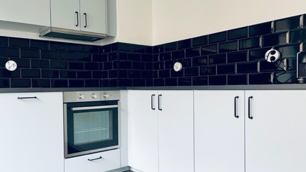 Una cucina con mobili bianchi, zoccolo a mosaico nero e forno a incasso.
