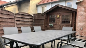 Un patio con un tavolo rettangolare e sei sedie, circondato da una recinzione in legno e un muro di mattoni.