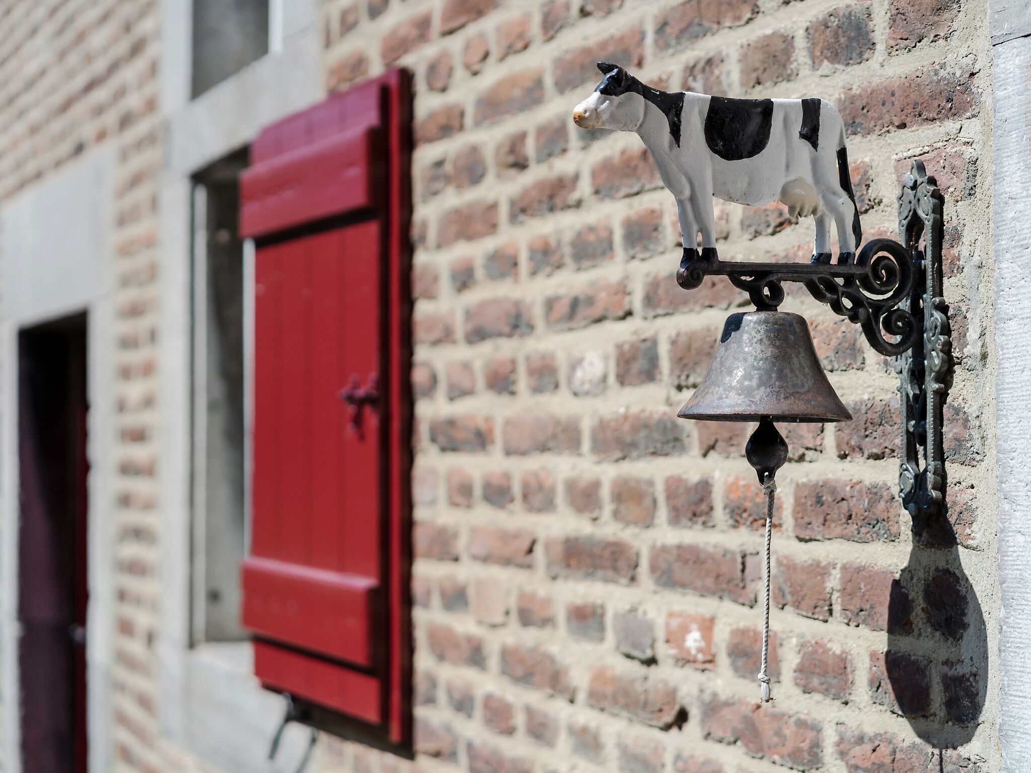 Une porte rouge avec une cloche en métal et une figurine en forme de vache fixée à un mur de briques.