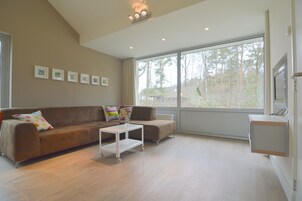 A modern living room with a brown sofa, a white coffee table, and a large window offering a view of trees.