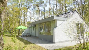 Et moderne hus med skråt tag, store glasruder og en terrasse med udendørs møbler.