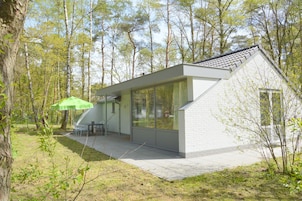 A modern house with a sloped roof, large glass windows, and a patio area with outdoor furniture.
