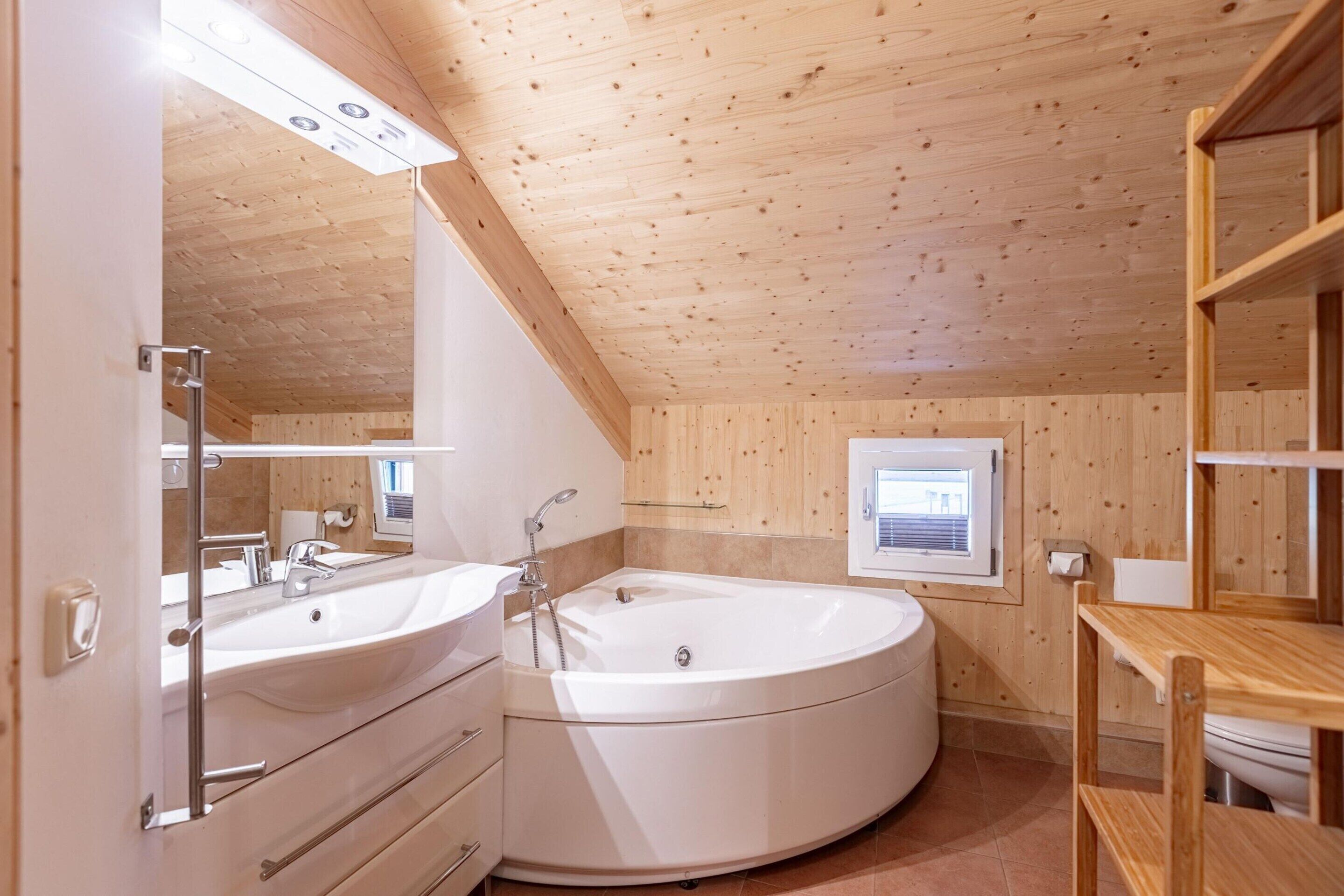A modern bathroom with two sinks, a large bathtub, wooden walls, and a skylight.