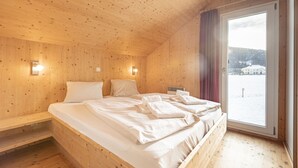 Una habitación de cabaña de madera con una cama, una ventana y vistas a un paisaje nevado.