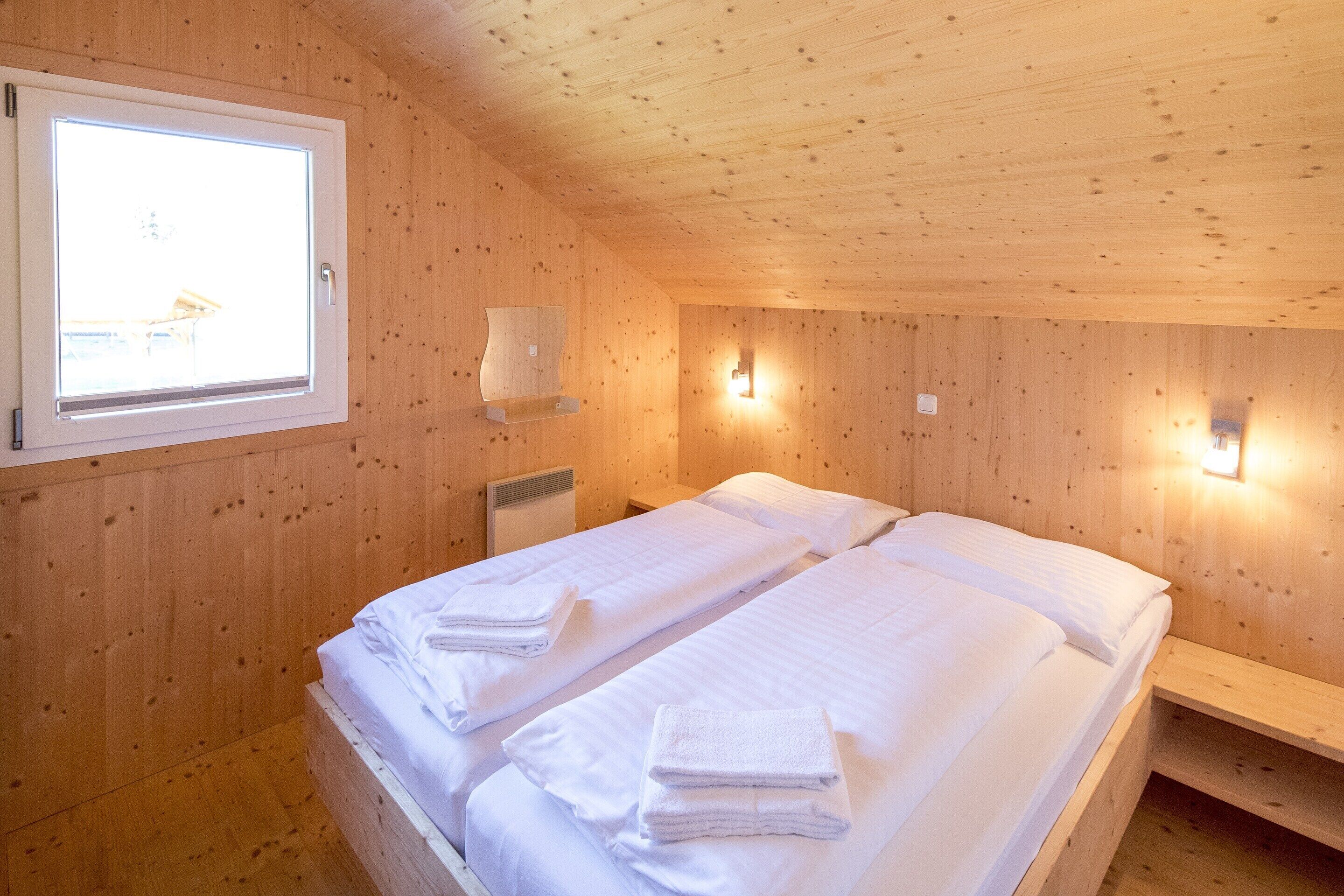 Ein Zimmer in einer Holzhütte mit zwei Betten, einem Fenster und Wandleuchten.