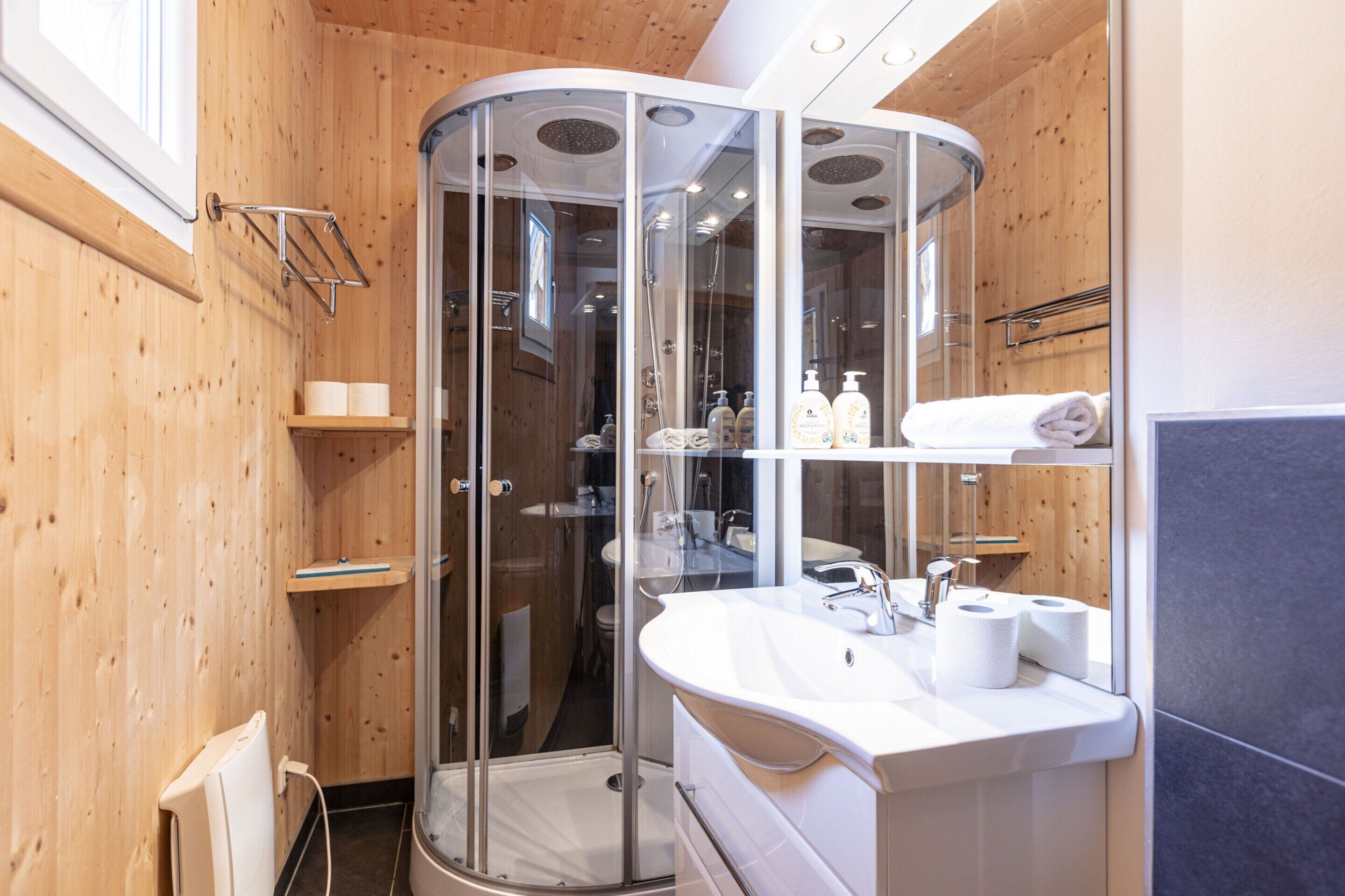Un baño moderno con ducha de vidrio, lavamanos blanco con espejo y paredes de madera.