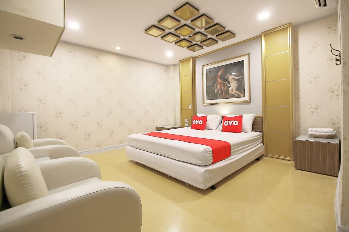 A hotel room with a bed, a sofa, a nightstand, and a painting on the wall.