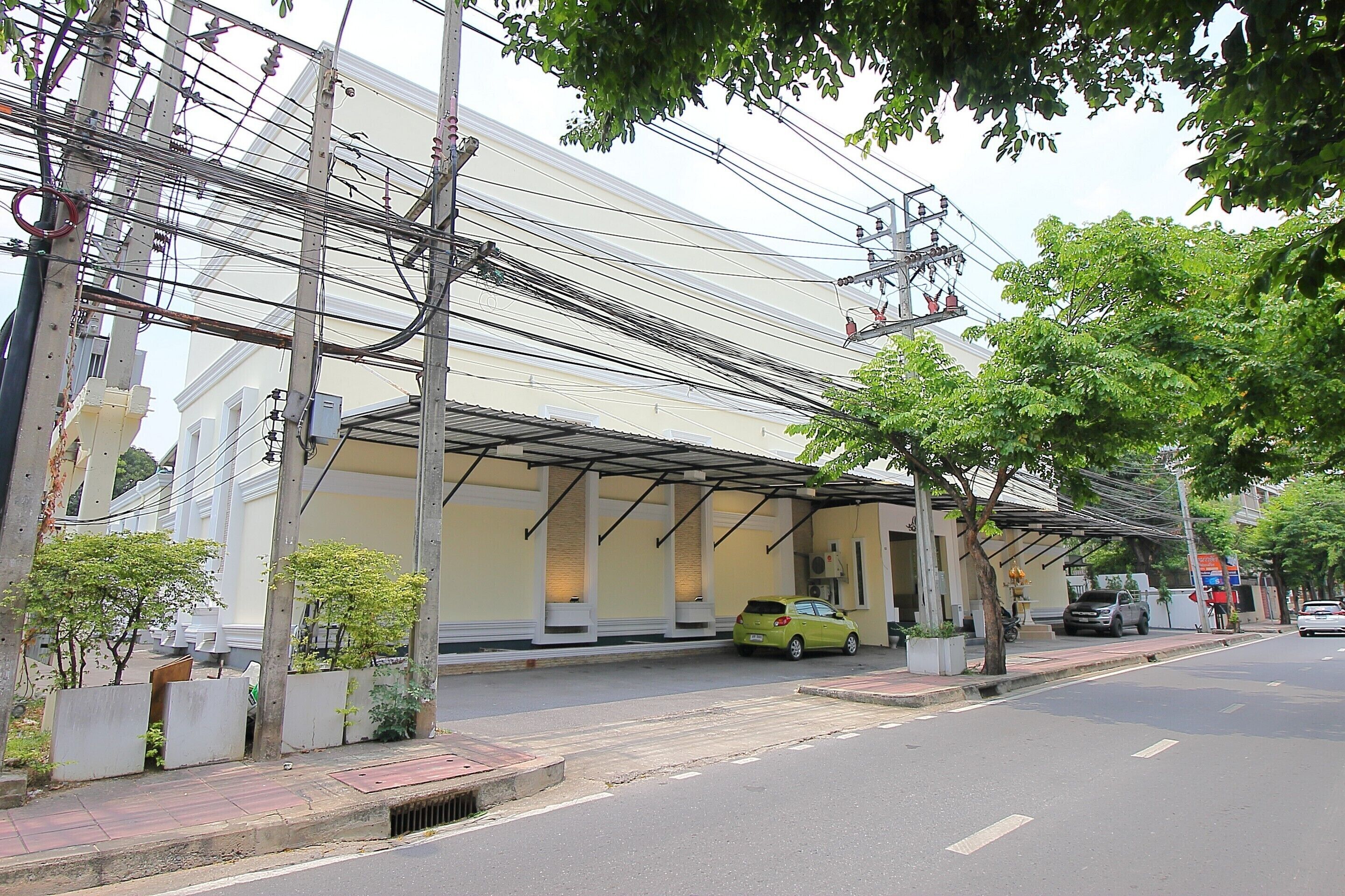 A building with a covered entrance, a parked car, and a sidewalk with trees.