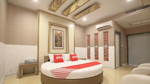 A hotel room with a round bed, a small bedside table, a wall-mounted air conditioner, and a door with a decorative panel. - OYO 1002 Pinklao Resort (Bangkok)