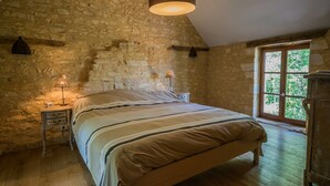 Ein Schlafzimmer mit Steinsandsteinwand, einem hölzernen Bett, einem Nachttisch mit Lampe und einem Fenster mit Ausblick.