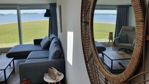 Ein modernes Zimmer mit einem großen Spiegel, einem grauen Sofa, einem kleinen Tisch und Seeblick.