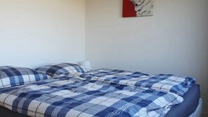 Ein Bett mit einer blau-weißen karierten Tagesdecke und passenden Kissen, ein weißes Kopfteil und ein rotes und weißes Bild an der Wand.