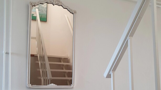 Eine Treppe mit weißen Geländern führt zu einer oberen Etage. Darunter an der Wand ist ein weißer Heizkörper angebracht.