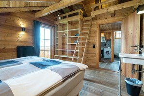 A wooden cabin interior with a bed, a ladder, a washing machine, and a sink.
