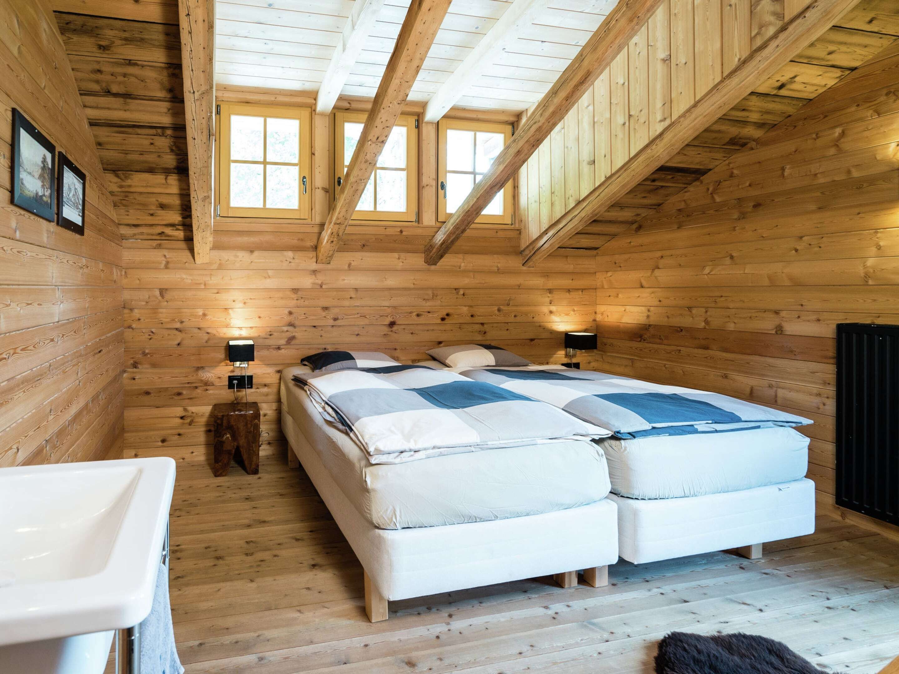 Une chambre confortable dans un chalet, avec deux lits, un plafond en bois et une petite salle de bain avec un lavabo.