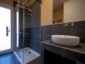 A modern bathroom with a glass shower enclosure, a white sink, and dark tiled walls. - Welcoming Chalet With hot tub (Sankt Georgen am Kreischberg)