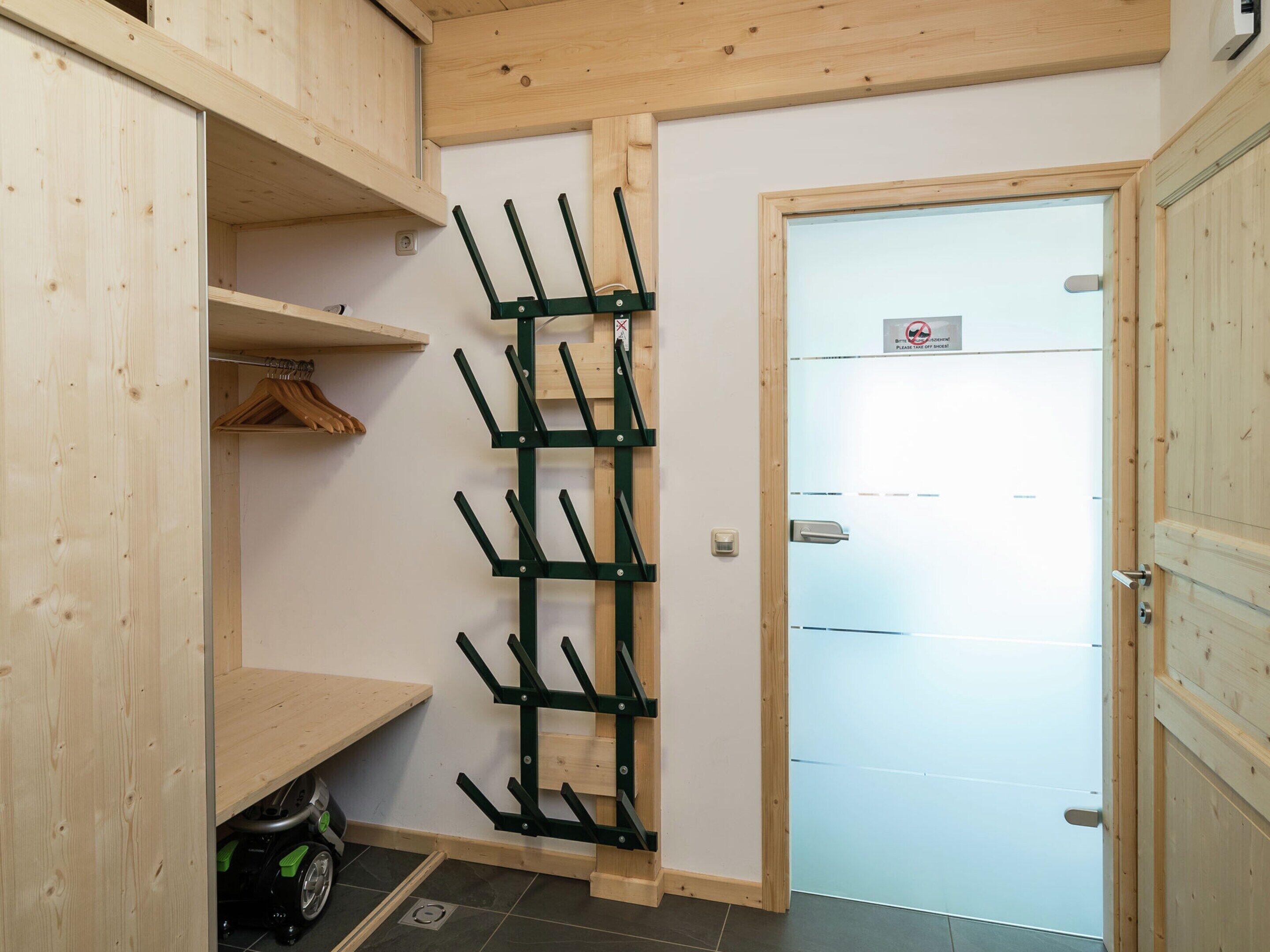 A wooden interior with a coat rack, a door with a sign, and a small table with a bag.