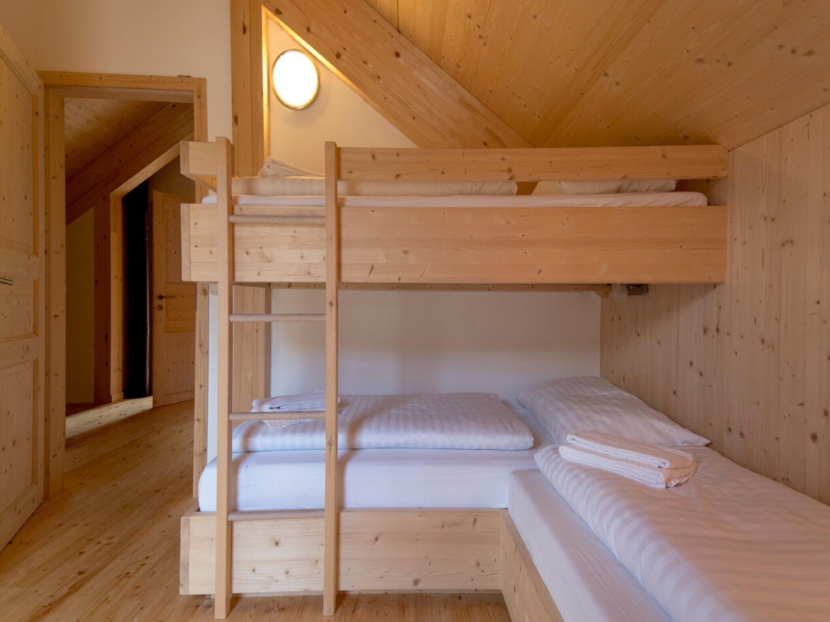 A wooden bunk bed room with a ladder, a small shelf, and a wall-mounted light.