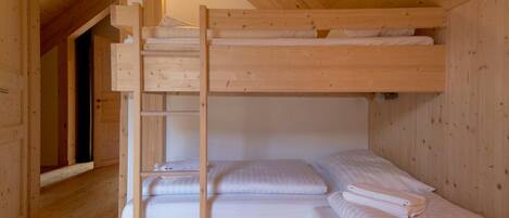 A wooden bunk bed room with a ladder, a small shelf, and a wall-mounted light.