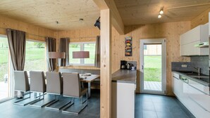 Eine moderne Küche mit Holzwänden, einem Essbereich mit Stühlen und einem Tisch sowie Blick ins Freie.