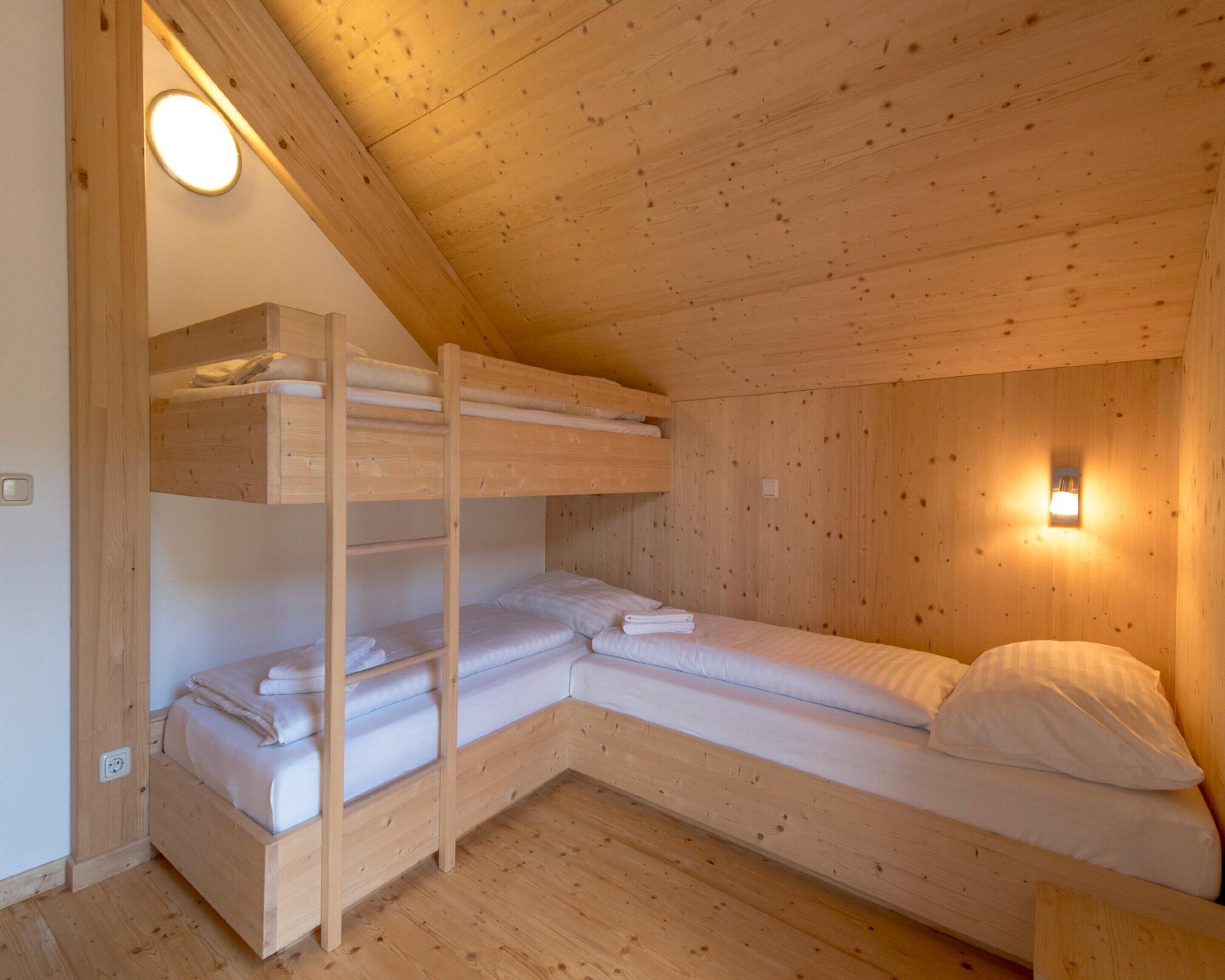 A wooden cabin room with bunk beds, a single bed, and a wall-mounted light fixture.