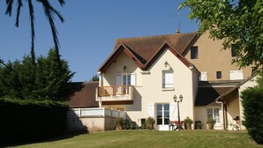Ein zweistöckiges Haus mit Balkon, einem kleinen Garten und blauem Himmel.