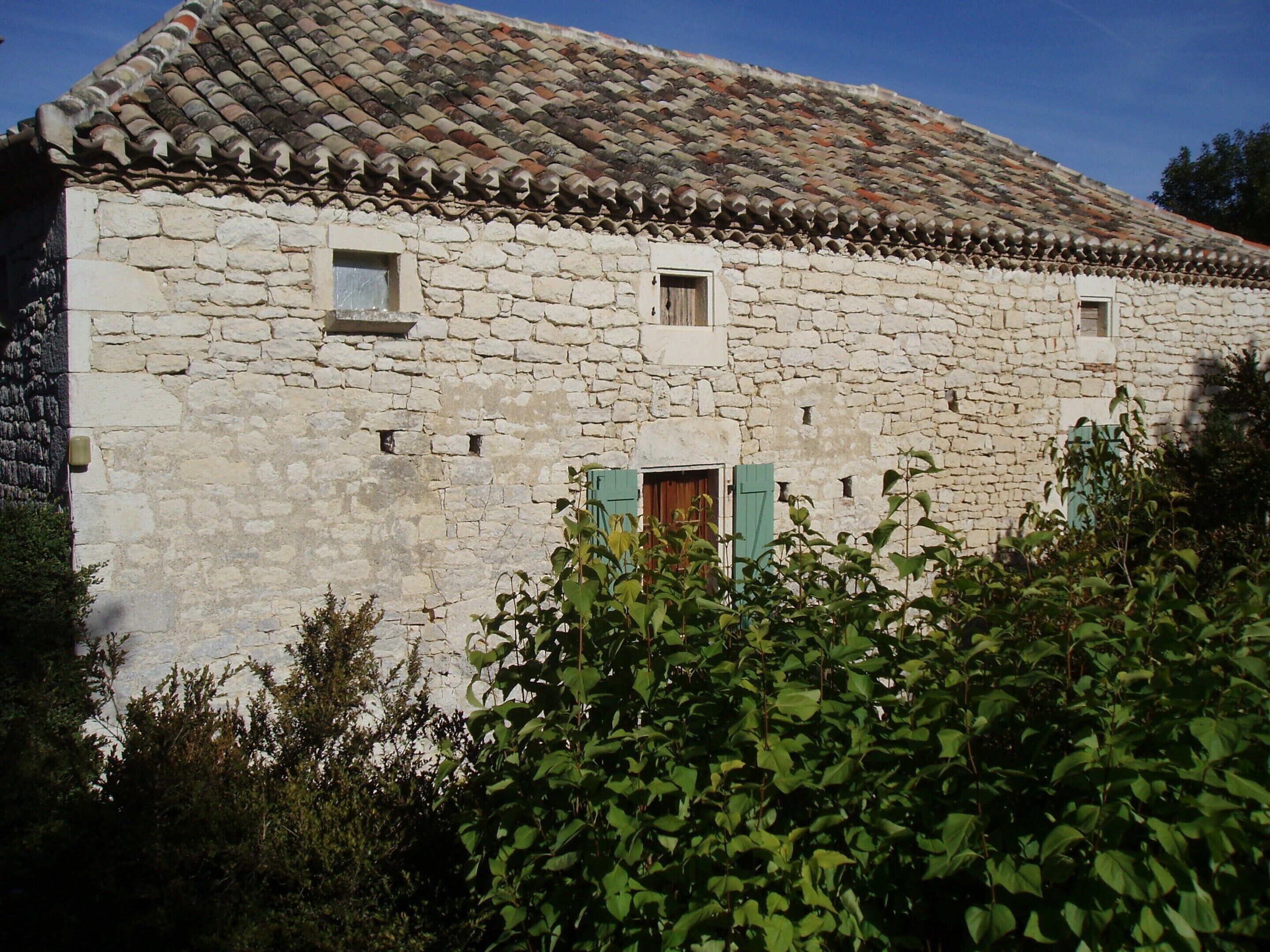 Un edificio de piedra con techo de tejas, dos ventanas pequeñas y una puerta de madera.