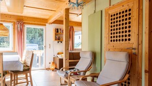A wooden interior with a dining table, two cushioned chairs, a bookshelf, and a door with a circular pattern. - Chalet in Dachstein West With Shared Pool (Annaberg-Lungoetz)