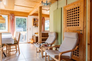 Interior de madera con una mesa de comedor, dos sillas acolchadas, una estantería y una puerta con un diseño circular.