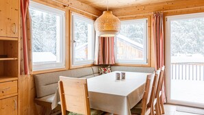 A cozy cabin interior with a wooden dining table, bench seating, and large windows offering a view of a snowy landscape. - Chalet in Dachstein West With Shared Pool (Annaberg-Lungoetz)